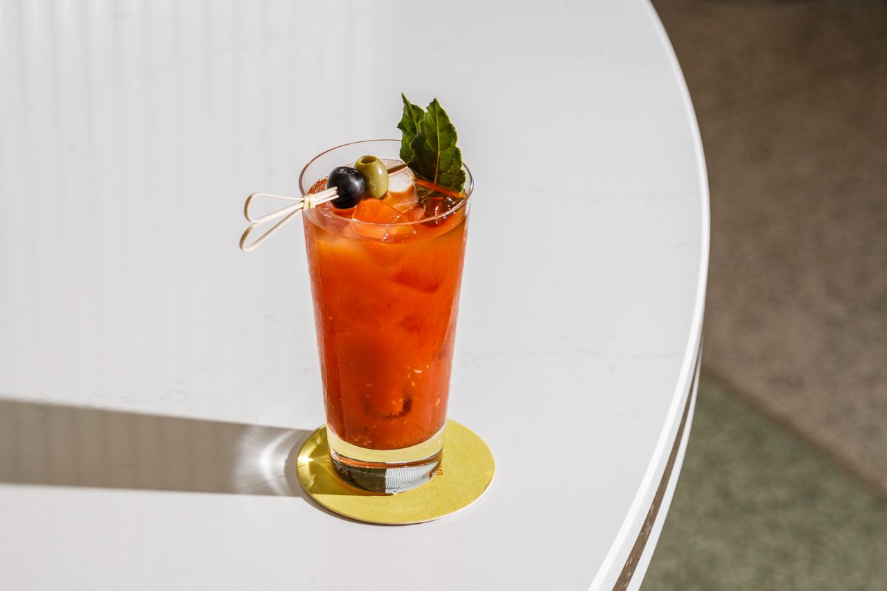 A close-up shot of a classic Bloody Mary cocktail garnished with olives and fresh herbs on a chic table.