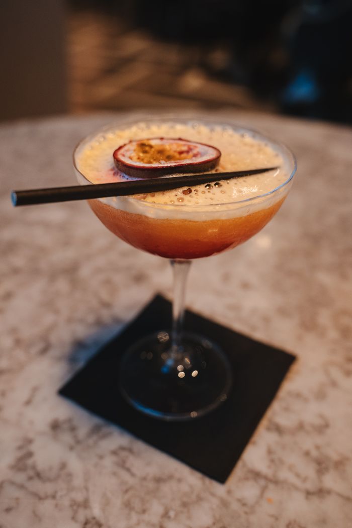 Close-up of a passion fruit martini with a slice garnish, served in an elegant glass on a marble table.