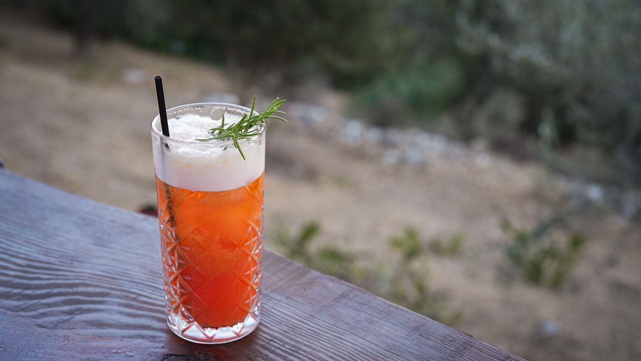 A vibrant citrus cocktail in a crystal glass with a rosemary garnish on an outdoor table.
