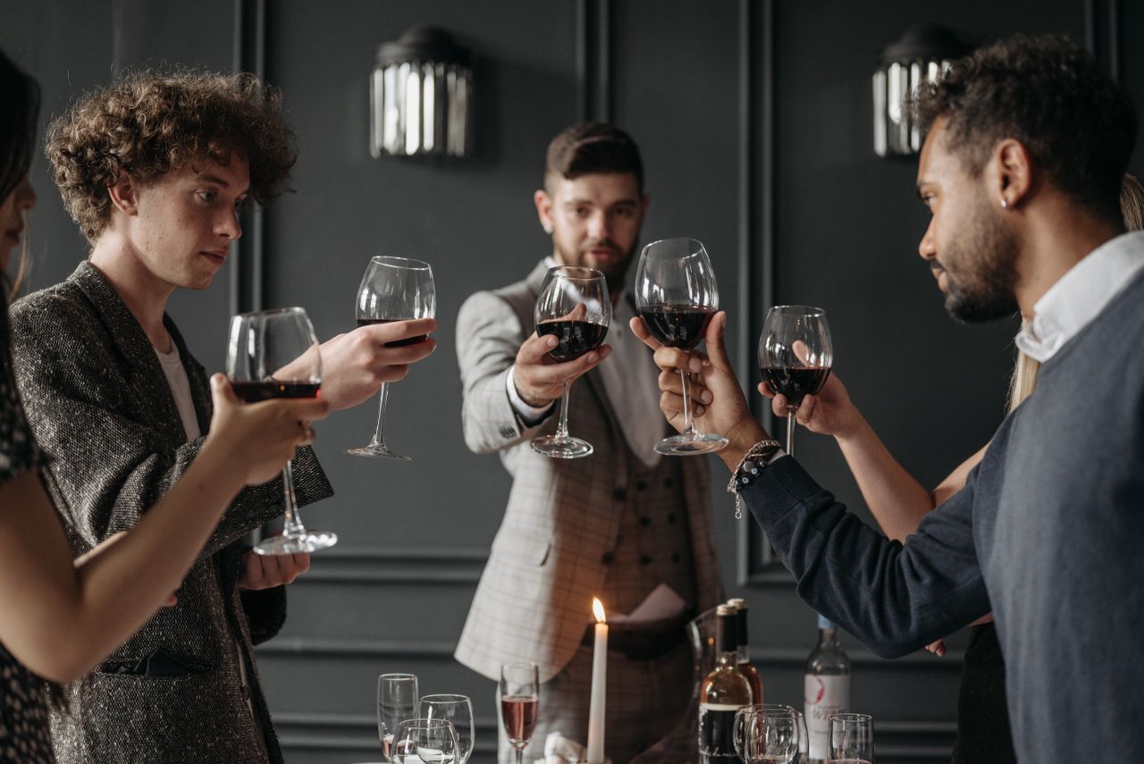 A group of elegantly dressed adults in suits toasting with red wine at a sophisticated party.